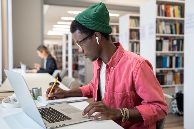 college student watching a recorded lecture on his laptop and taking notes